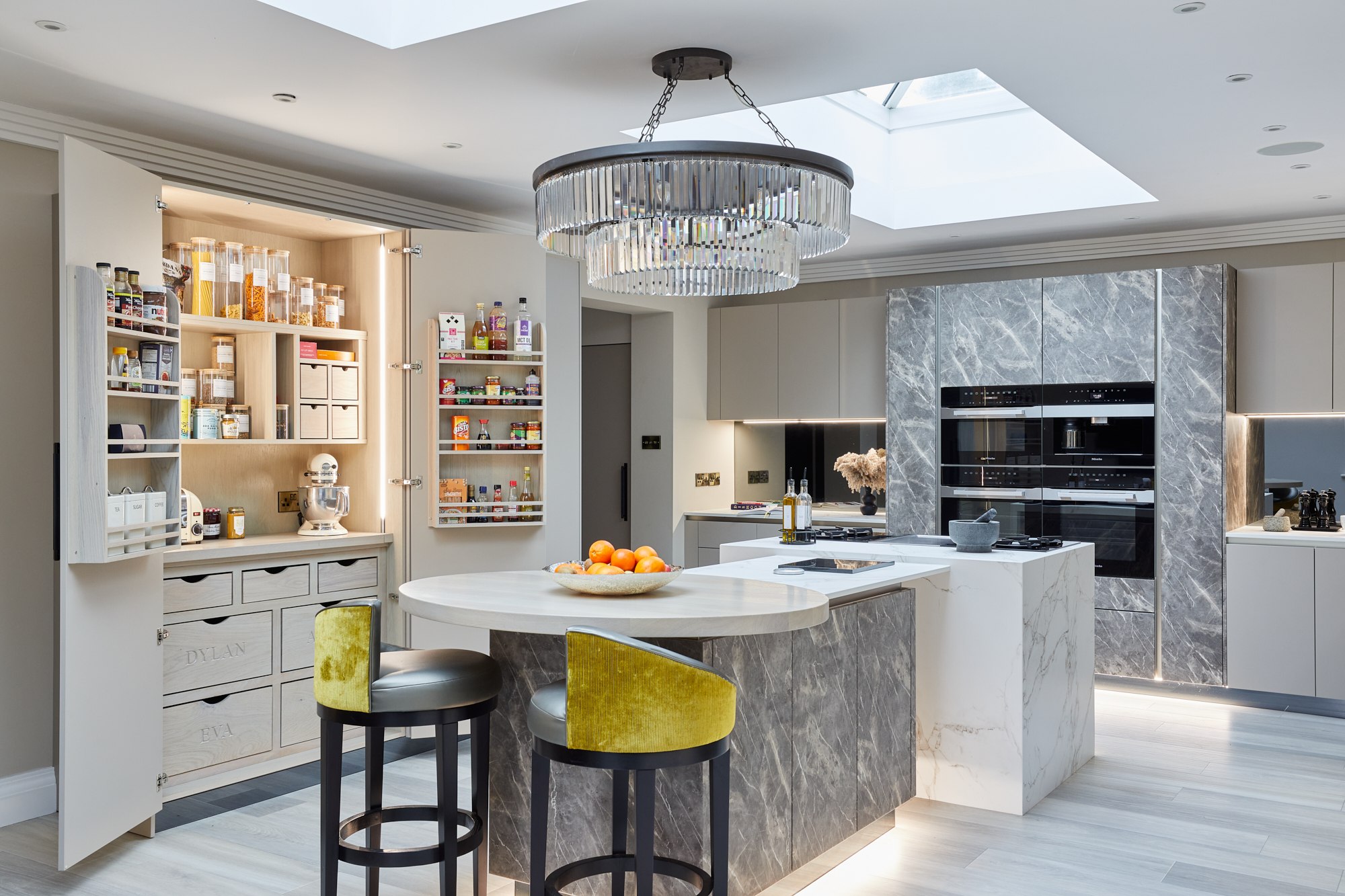 The Sculpted Kitchen: illuminated open pantry beside the stone-effect island and curved breakfast bar